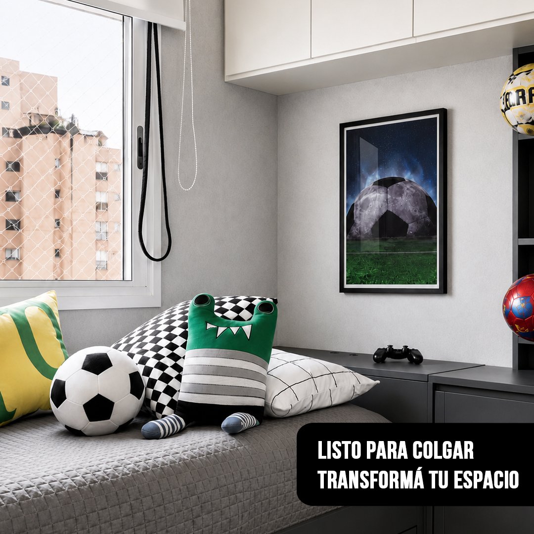 Cuadro vertical enmarcado en negro de una pelota de fútbol con textura de luna sobre una cancha, colgado en una habitación juvenil con almohadones temáticos de deporte y un joystick en el escritorio