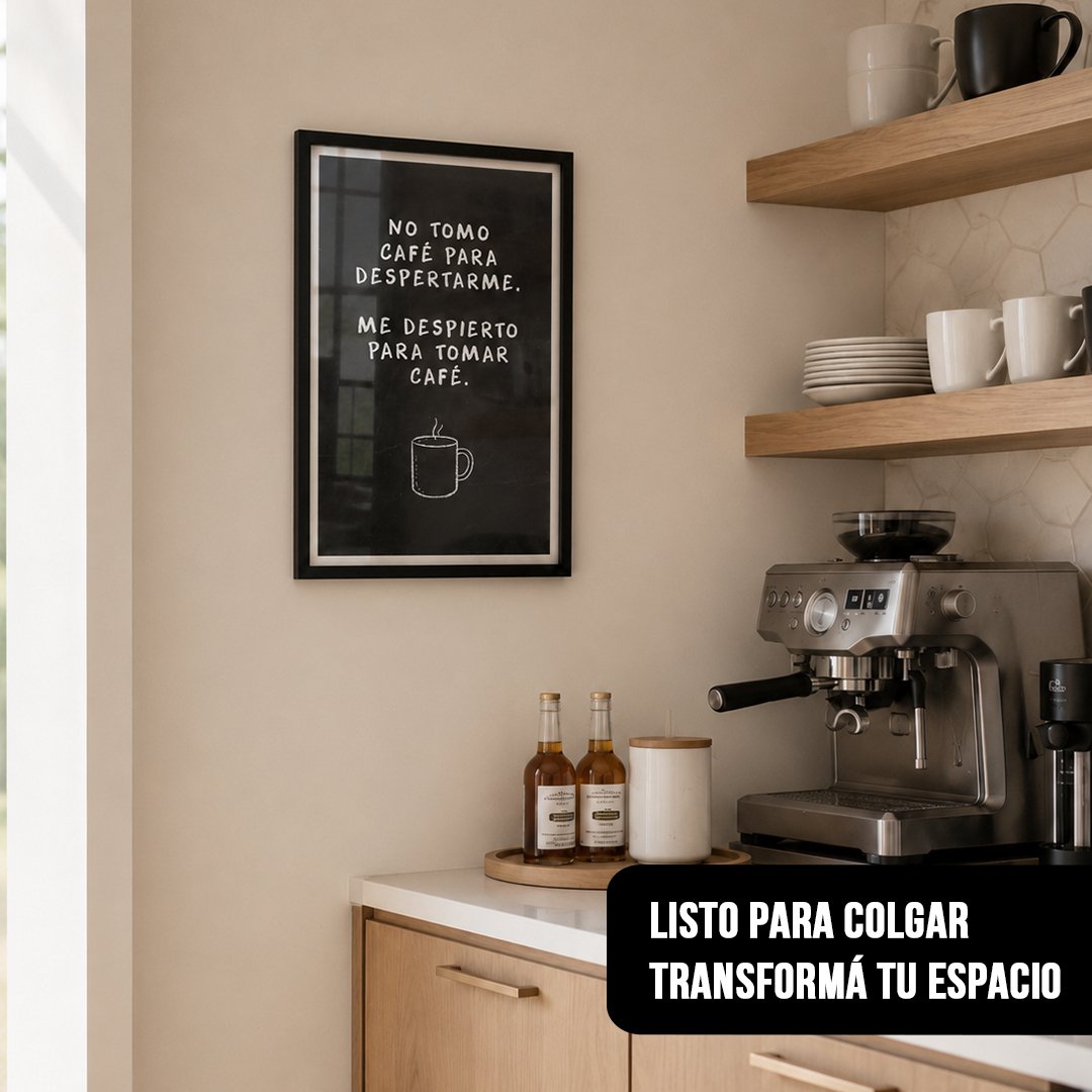 Cuadro vertical enmarcado en negro con una frase sobre café escrita en una pizarra, colgado en una cocina moderna al lado de estantes flotantes de madera y una cafetera espresso
