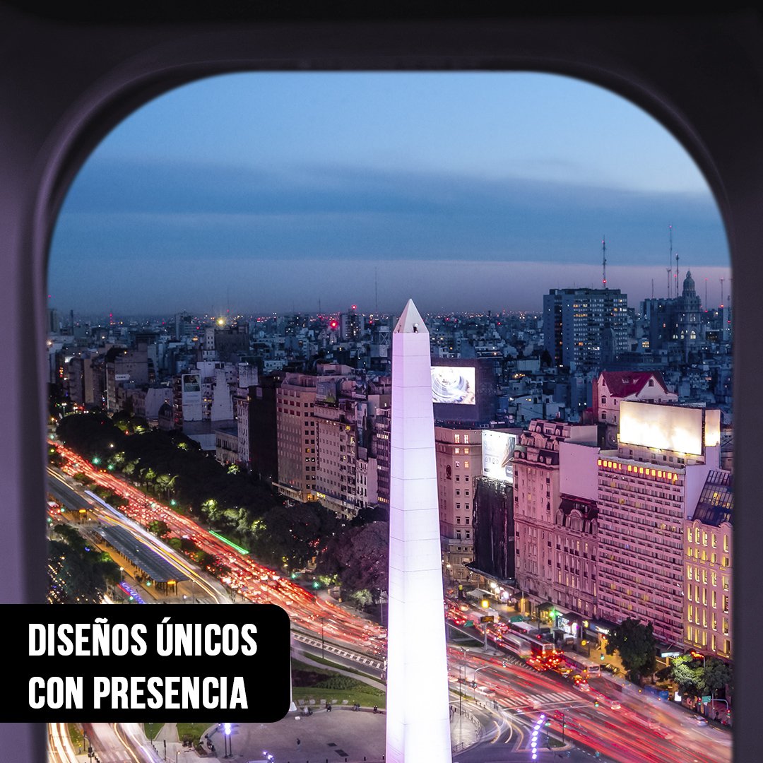 Fotografía aérea nocturna del Obelisco y la Avenida 9 de Julio con estelas de luces de tráfico, vista a través de la ventanilla de un avión