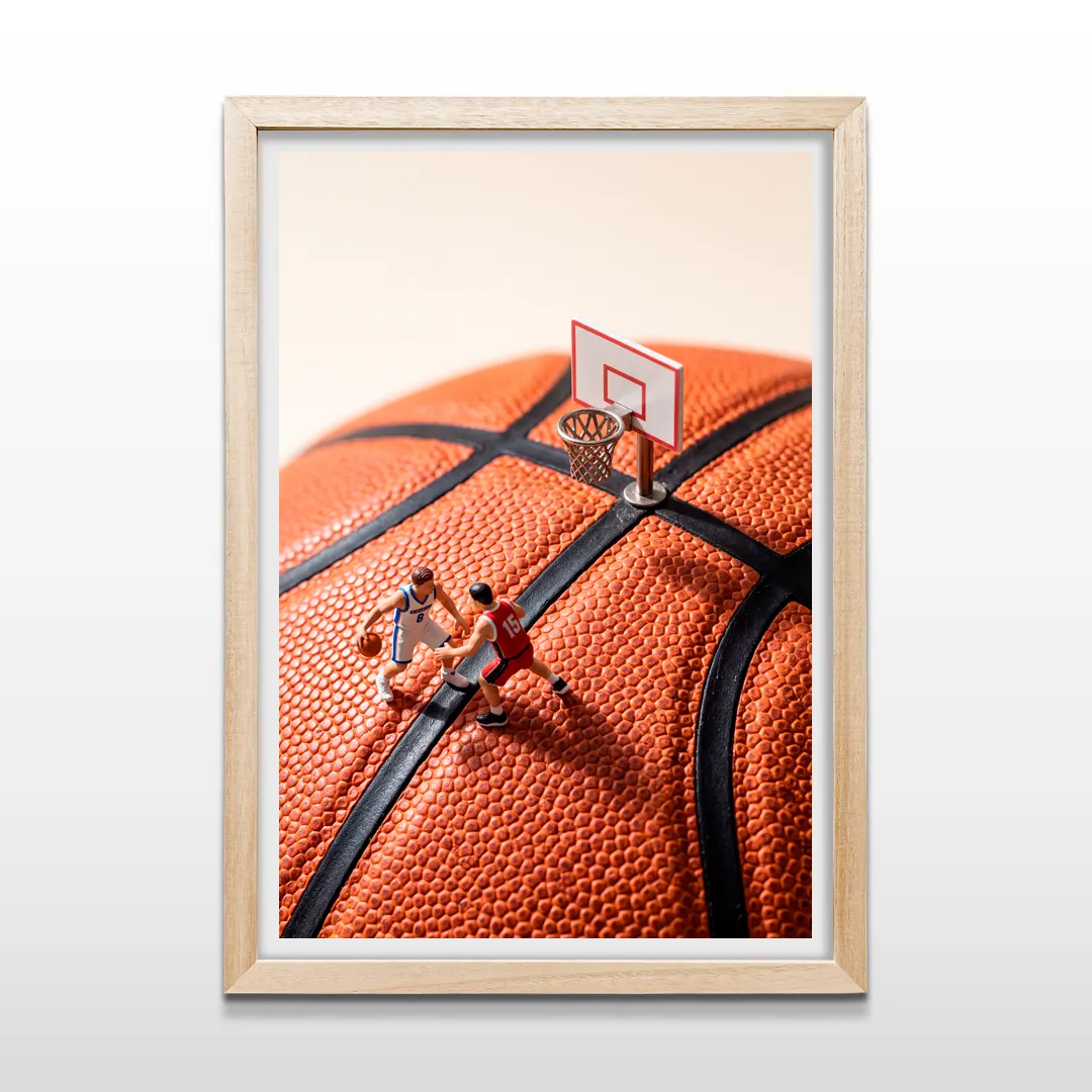 Cuadro vertical en marco de madera clara con foto macro de jugadores diminutos y aro montado sobre balón de baloncesto