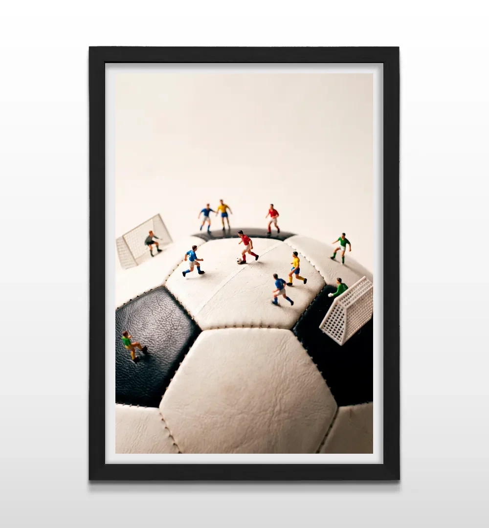 Cuadro vertical en marco negro con lámina fotográfica creativa de futbolistas en miniatura sobre balón blanco y negro
