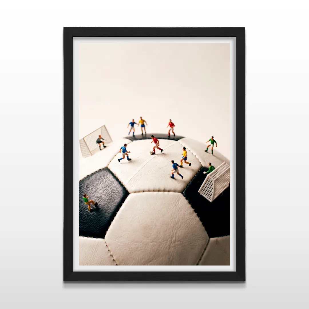 Cuadro vertical en marco negro con lámina fotográfica creativa de futbolistas en miniatura sobre balón blanco y negro